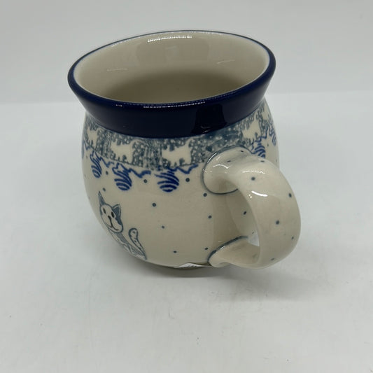 Elevated three-quarter view of a Ceramika Artystyczna Polish pottery bubble mug, highlighting a dotted right handle, a speckled blue cat motif, and a smooth off-white interior.
