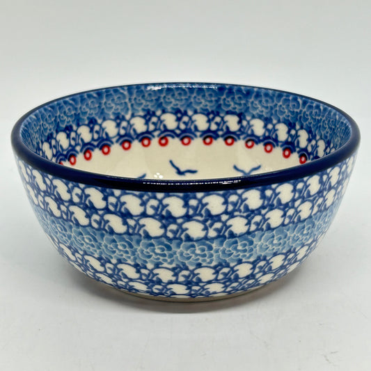 Slightly elevated front view of a Ceramika Artystyczna Polish pottery cereal bowl, highlighting the fully wrapped traditional blue and white stamped exterior pattern, dark blue rim, and interior red dot accents with flying seagulls.