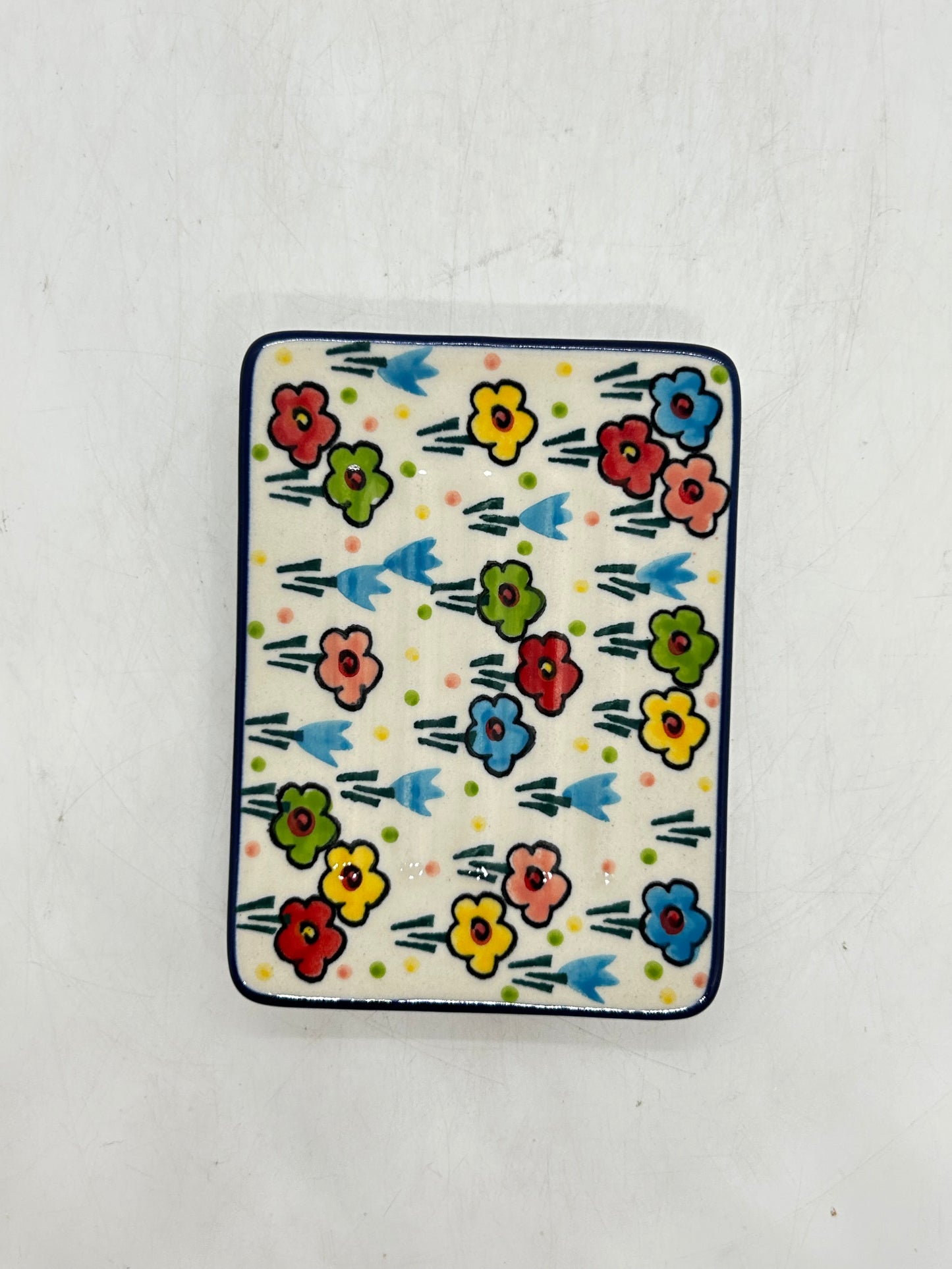 Direct overhead view of a Ceramika Artystyczna Polish pottery rectangular soap dish showing a dark blue border and hand-painted multi-colored spring flowers across the ridged surface.