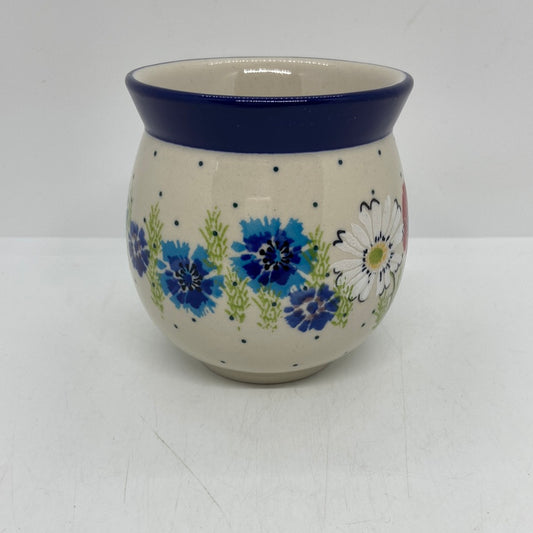 Straight-on view of the back of a Ceramika Artystyczna Polish pottery bubble mug, showing blue cornflowers, green stems, a dotted cream background, and a solid dark blue rim with no handle visible.