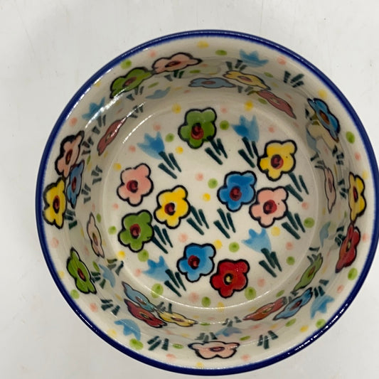 High-angle top-down view looking into a Ceramika Artystyczna Polish pottery ramekin, showing a solid dark blue rim and a fully decorated interior basin featuring hand-painted multi-colored spring flowers.