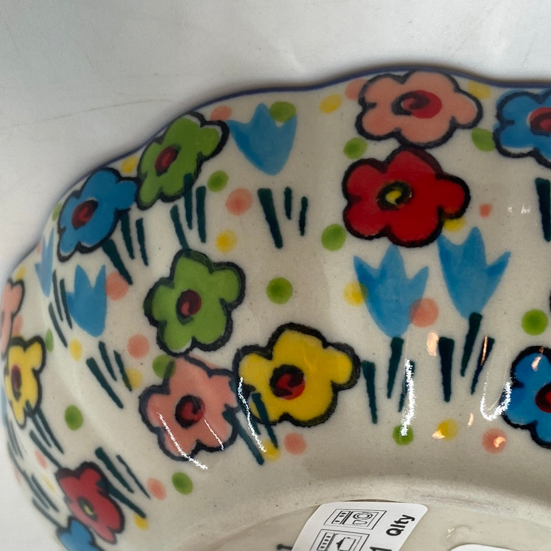 Extreme close-up of the fluted exterior wall of a Ceramika Artystyczna Polish pottery scalloped bowl, highlighting the high-gloss glaze and hand-painted multi-colored spring flowers near the base.