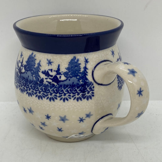 Three-quarter view of a Ceramika Artystyczna Polish pottery bubble mug with a right handle, featuring a hand-painted blue winter village, stars, and a solid dark blue rim.