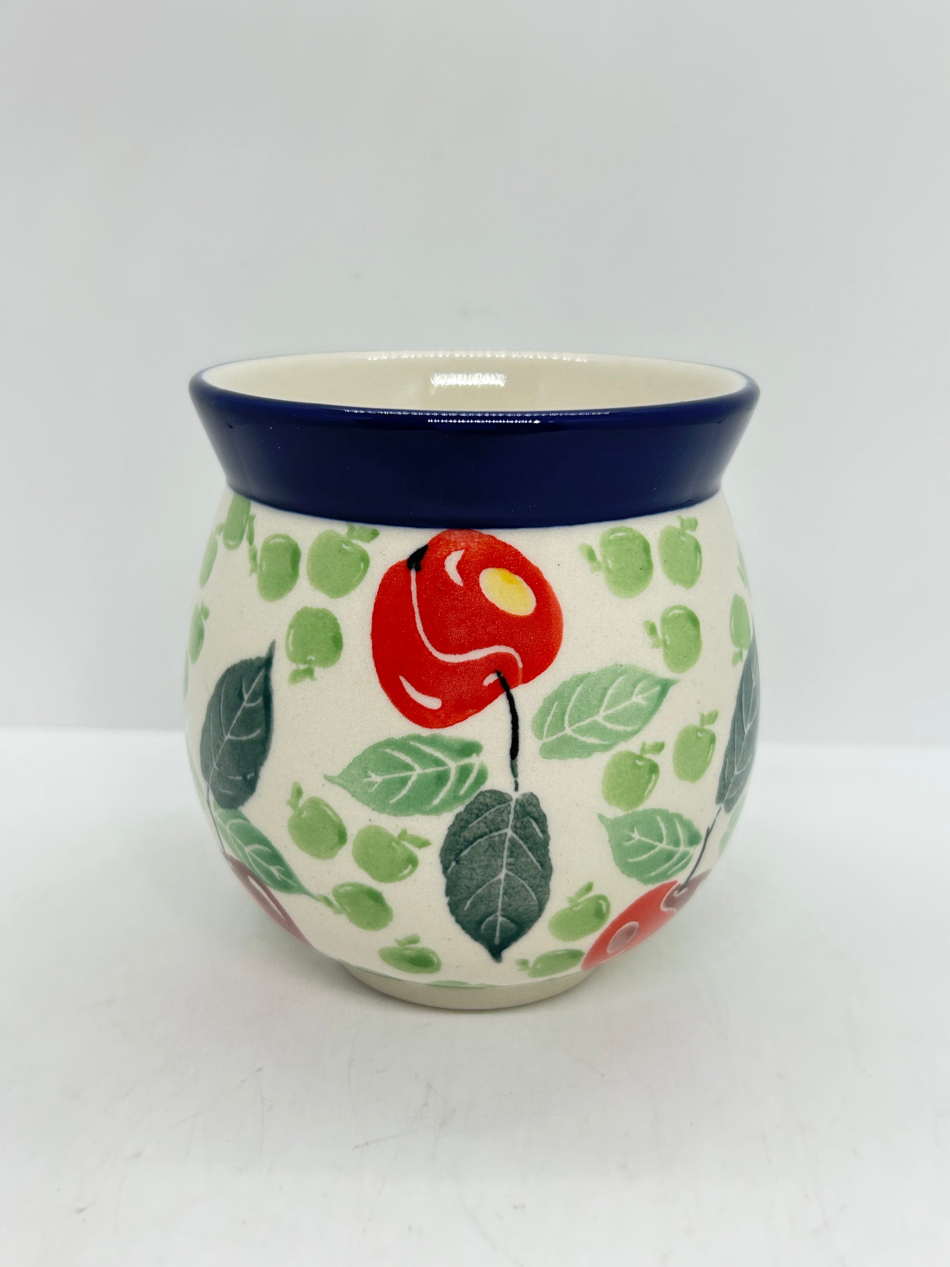 Straight-on view of the back of a Ceramika Artystyczna Polish pottery bubble mug, showing a continuous pattern of red and green apples, green leaves, and a solid dark blue rim with no handle visible.