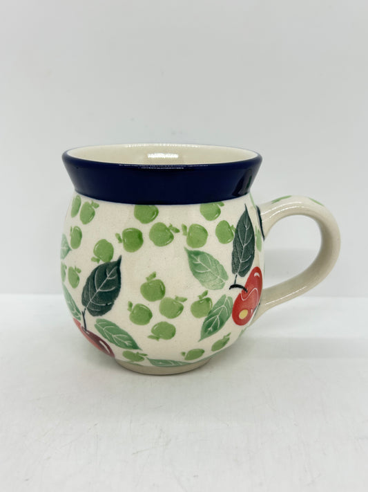 Straight-on side profile of a Ceramika Artystyczna Polish pottery bubble mug with the handle on the right, featuring hand-painted red and green apples, green leaves, and a solid dark blue rim.