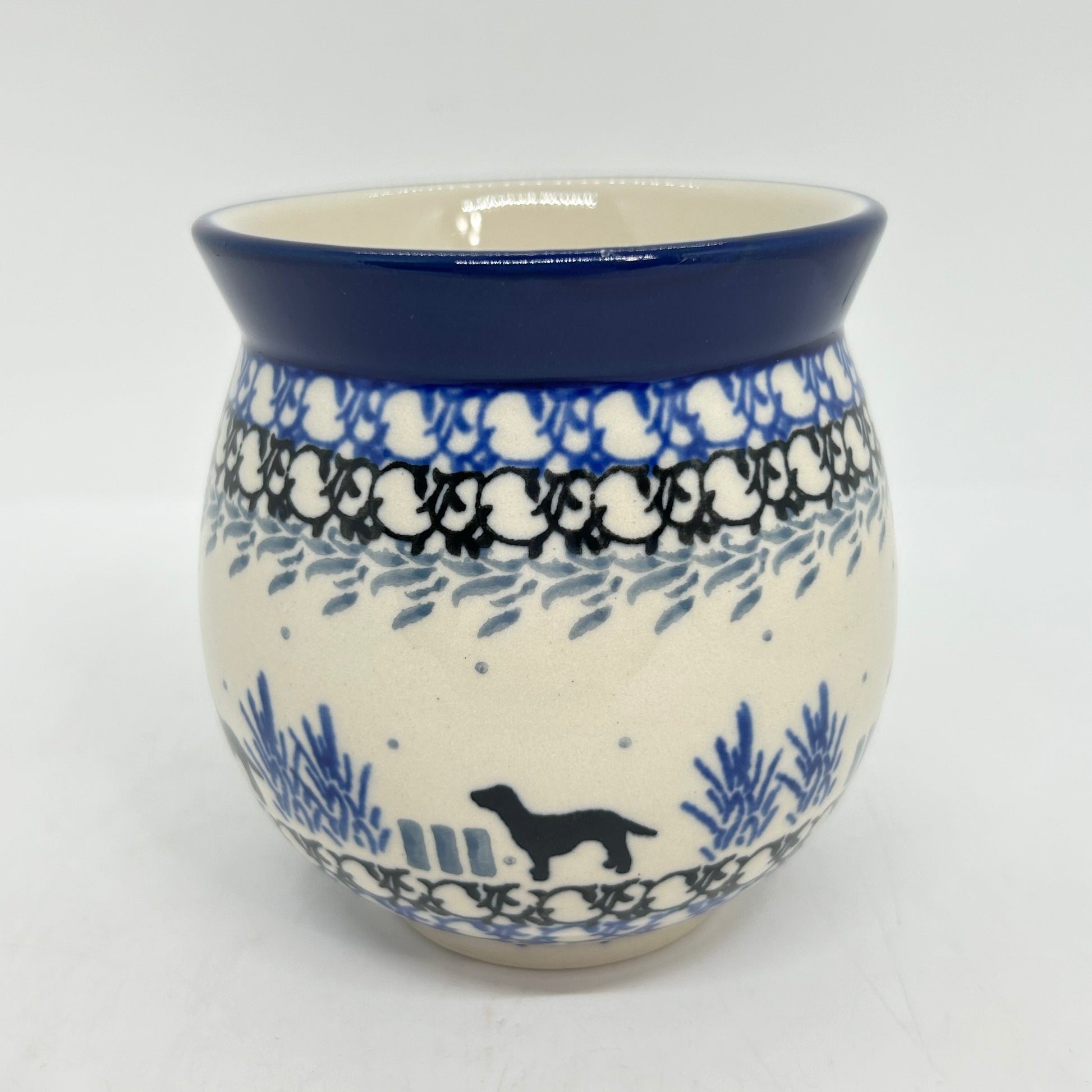 Straight-on view of the back of a Ceramika Artystyczna Polish pottery bubble mug, showing a black dog silhouette, blue plants, layered borders, and a solid dark blue rim with no handle visible.
