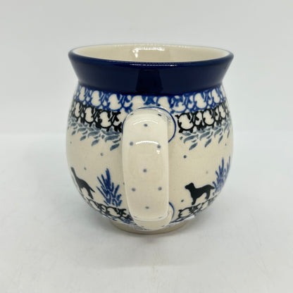 Straight-on view focusing on the dotted handle of a Ceramika Artystyczna Polish pottery bubble mug, flanked by black dog silhouettes, blue plant motifs, and complex layered borders.