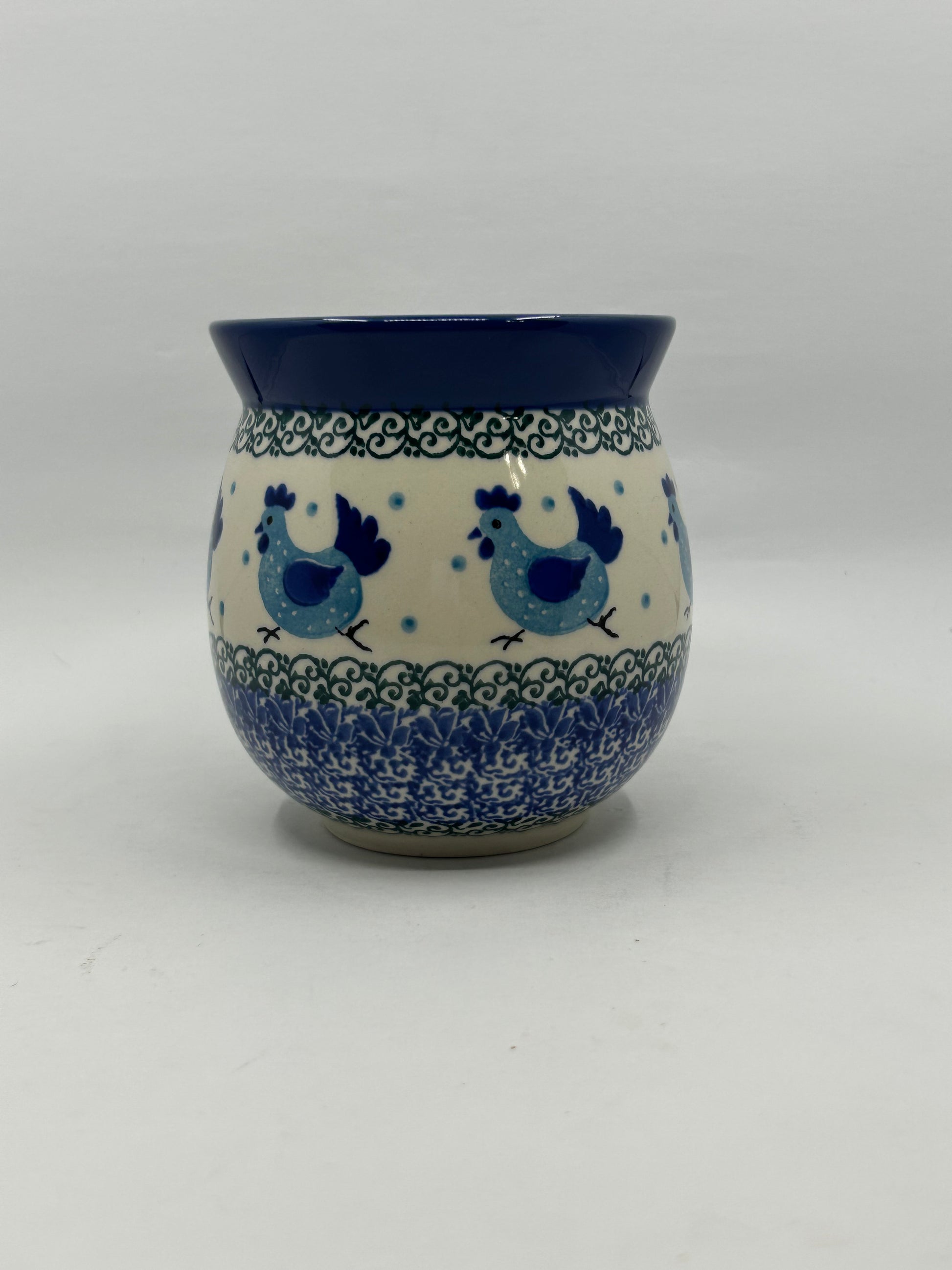 Straight-on view of the back of a Ceramika Artystyczna Polish pottery bubble mug, showing a continuous pattern of hand-painted blue chickens, green vine borders, dense blue stamping, and a solid dark blue rim with no handle visible.