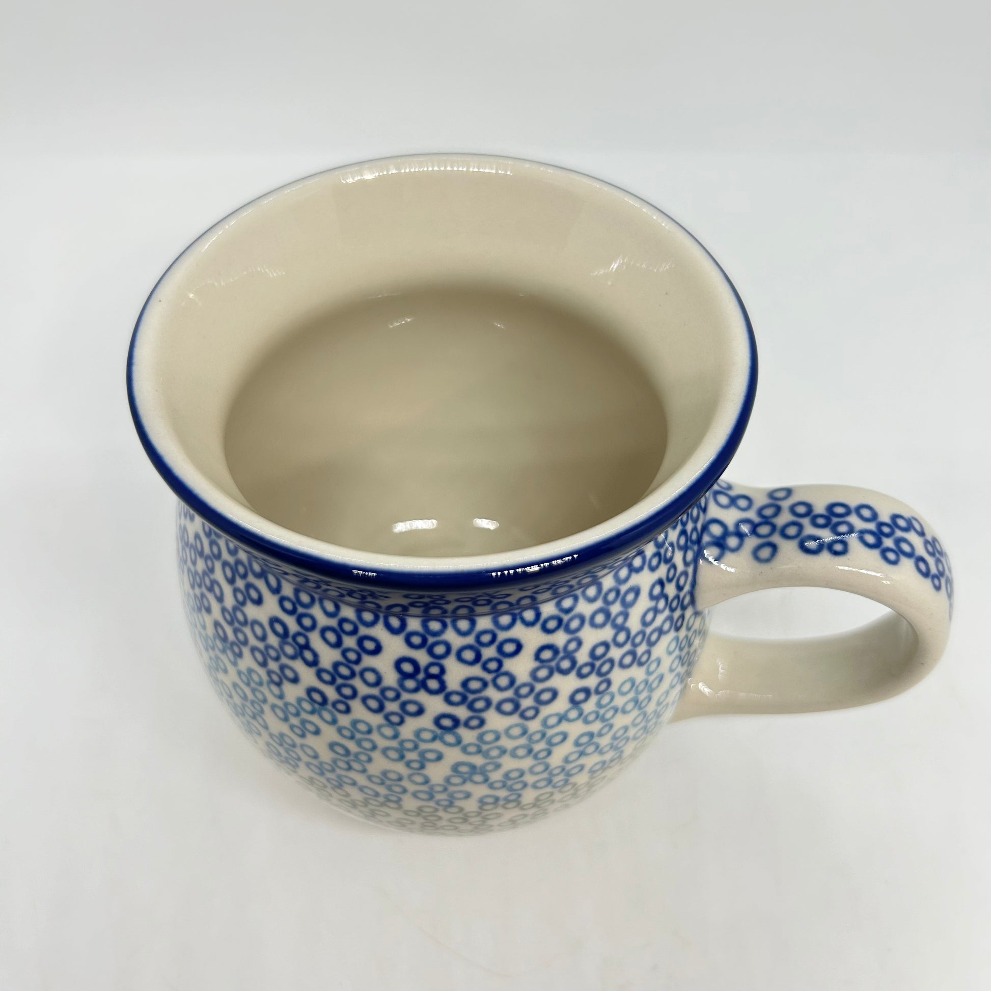 Elevated top-down view of a Ceramika Artystyczna Polish pottery bubble mug, showing a clean cream interior, a thin dark blue rim, and an exterior covered in small blue stamped circles.