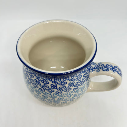 Elevated top-down view of a Ceramika Artystyczna Polish pottery bubble mug, showing a clean cream interior, a thin dark blue rim, and an exterior covered in small blue stamped circles.