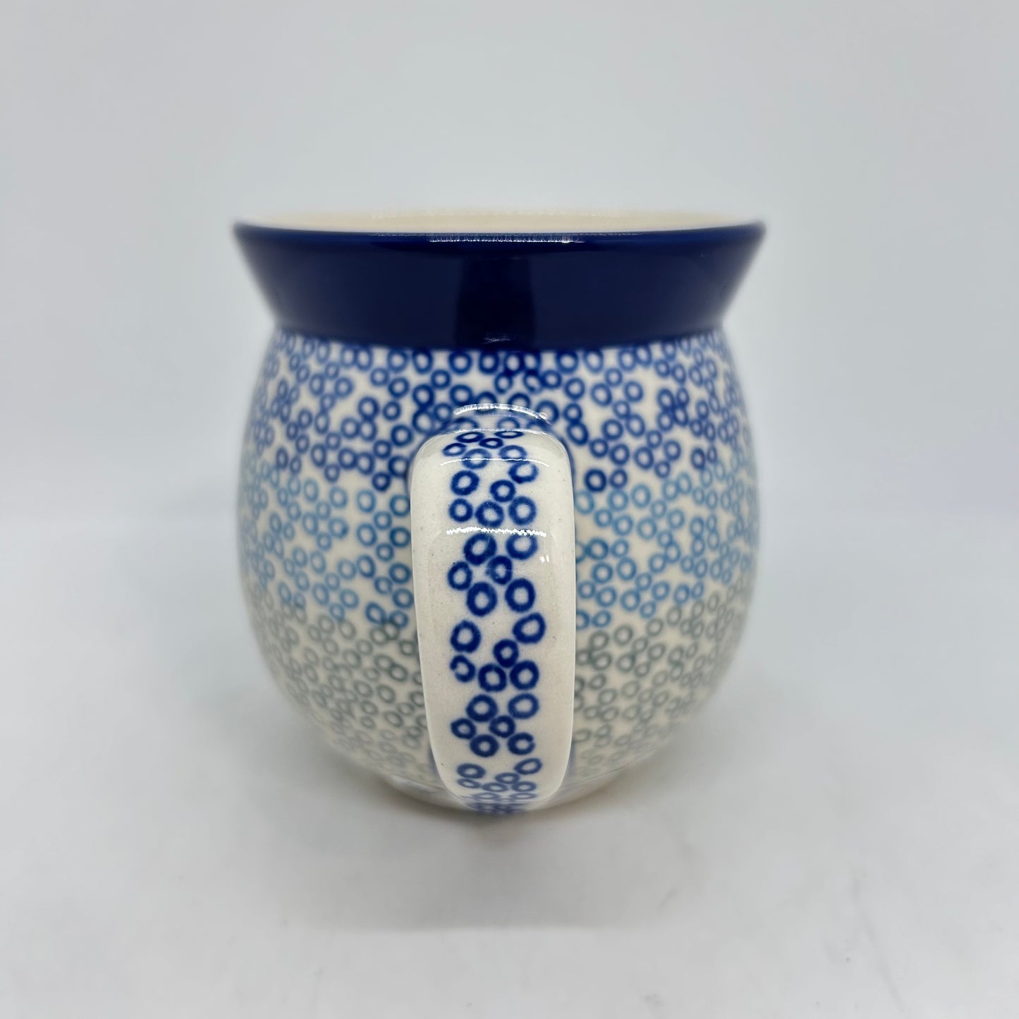 Straight-on view focusing on the dotted handle of a Ceramika Artystyczna Polish pottery bubble mug, flanked by a gradient pattern of blue and grey stamped circles, and a solid dark blue rim.