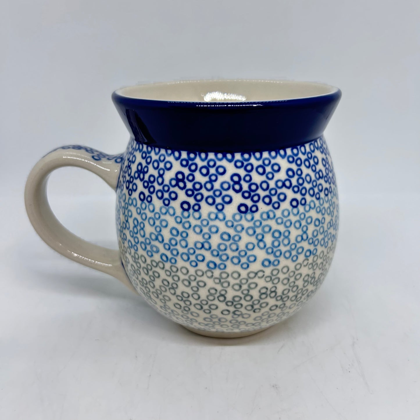 Straight-on side profile of a Ceramika Artystyczna Polish pottery bubble mug with the handle on the left, featuring a gradient pattern of dark blue, light blue, and grey stamped circles below a solid dark blue rim.