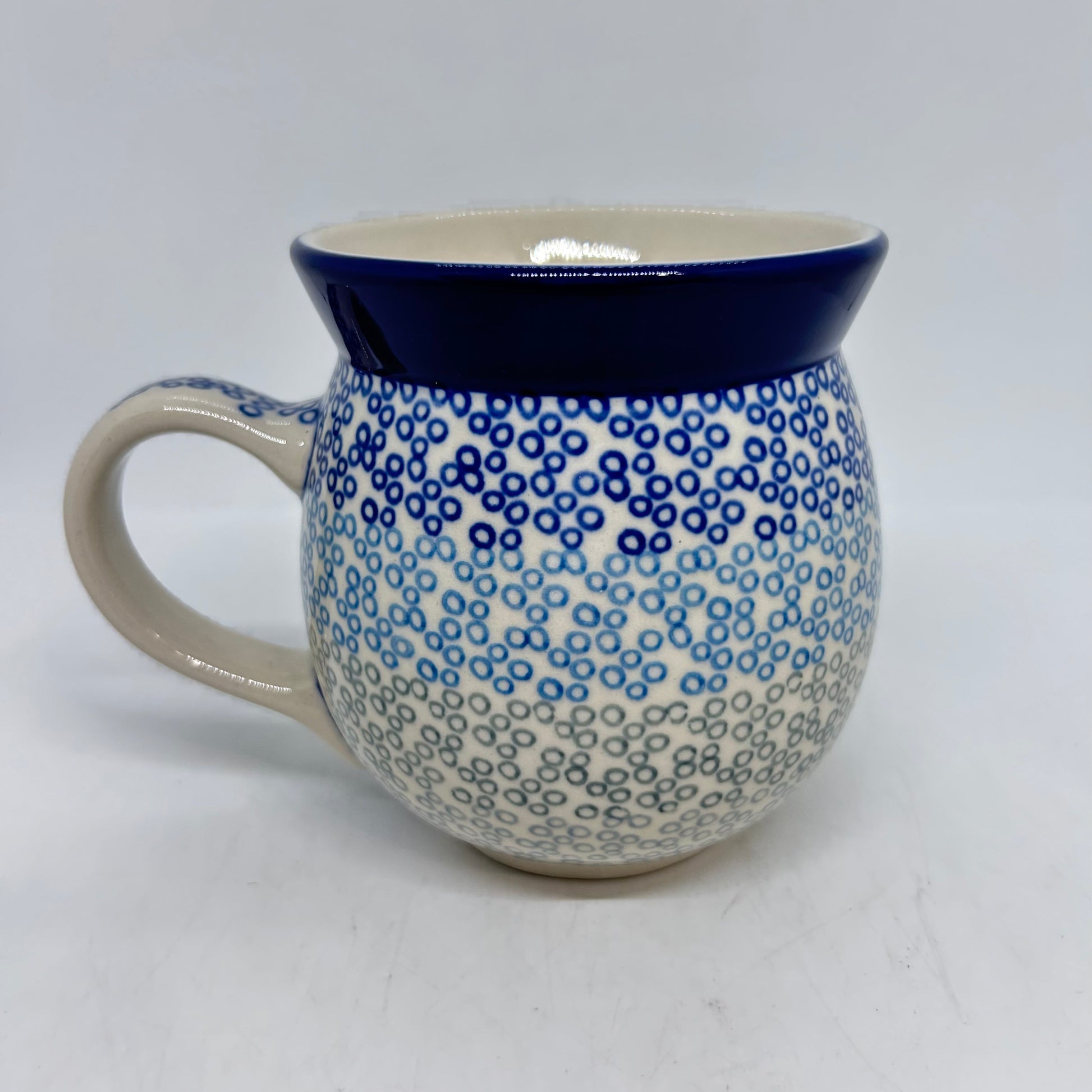 Straight-on side profile of a Ceramika Artystyczna Polish pottery bubble mug with the handle on the left, featuring a gradient pattern of dark blue, light blue, and grey stamped circles below a solid dark blue rim.