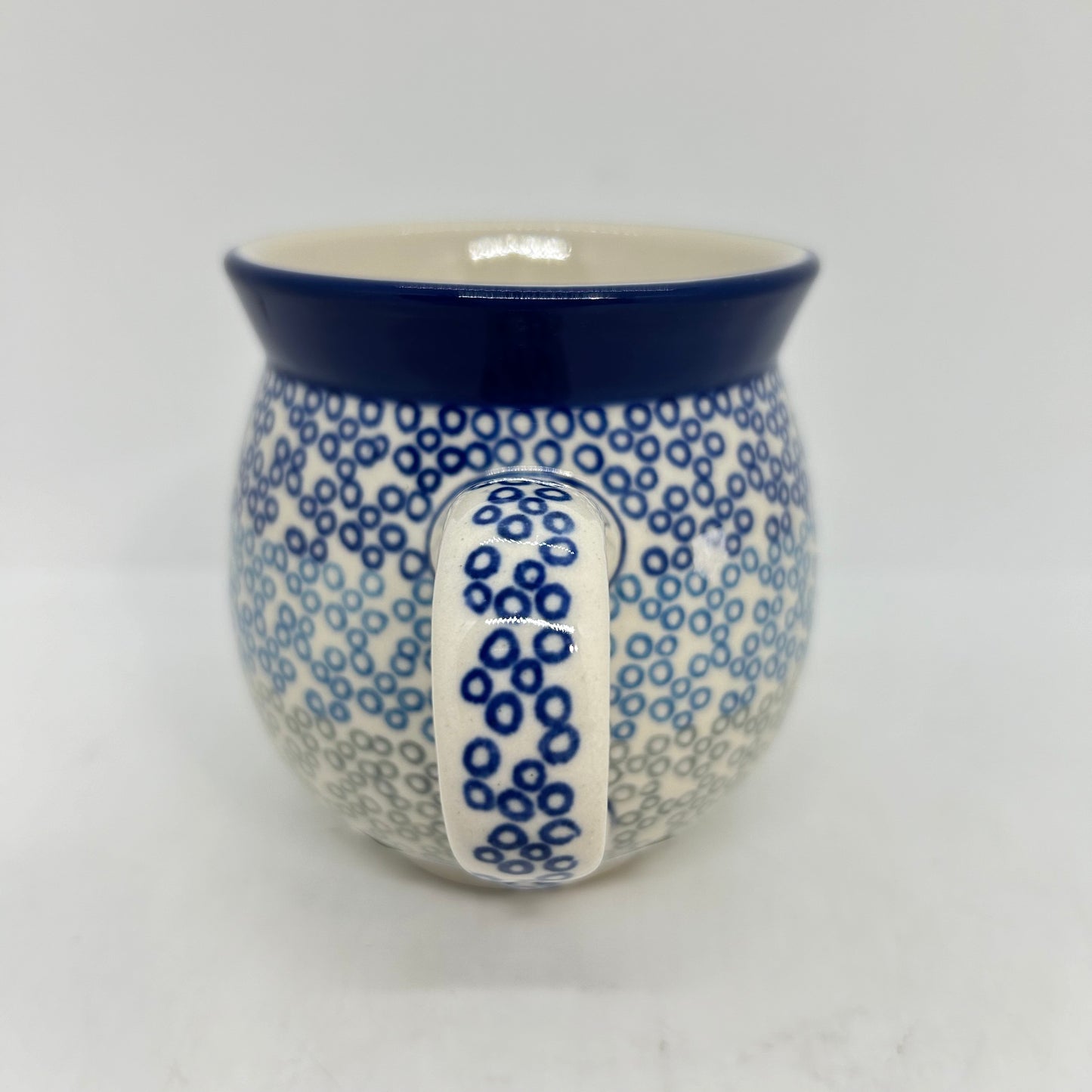 Straight-on view focusing on the patterned handle of a Ceramika Artystyczna Polish pottery bubble mug, flanked by a gradient pattern of blue and grey circular rings and a solid dark blue rim.