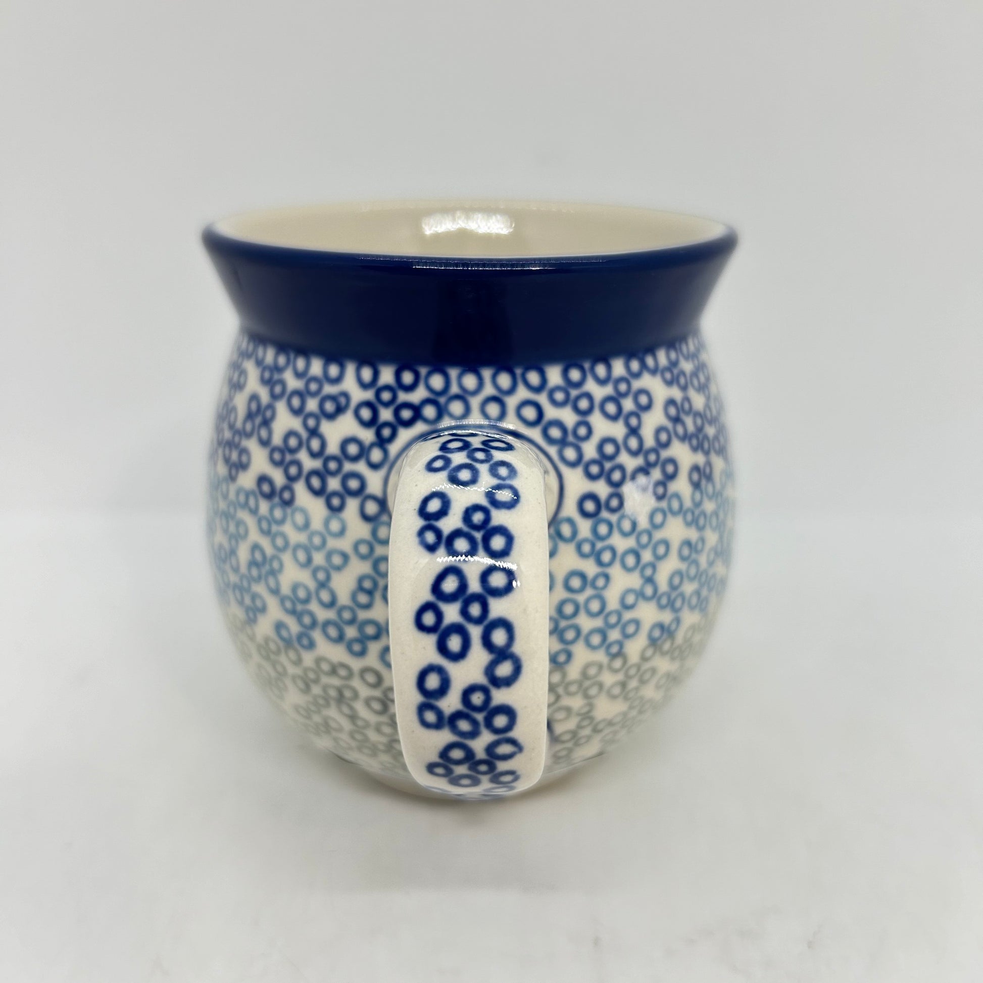 Straight-on view focusing on the patterned handle of a Ceramika Artystyczna Polish pottery bubble mug, flanked by a gradient pattern of blue and grey circular rings and a solid dark blue rim.