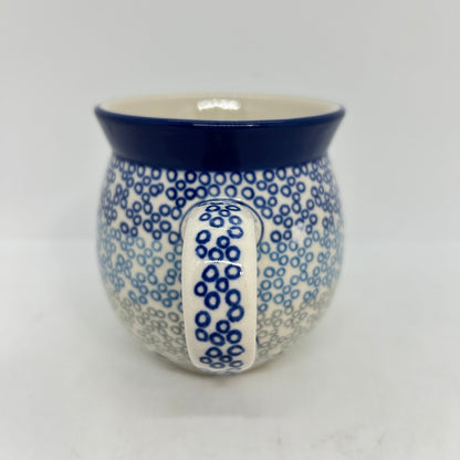 Straight-on view focusing on the patterned handle of a Ceramika Artystyczna Polish pottery bubble mug, flanked by a gradient pattern of blue and grey circular rings and a solid dark blue rim.