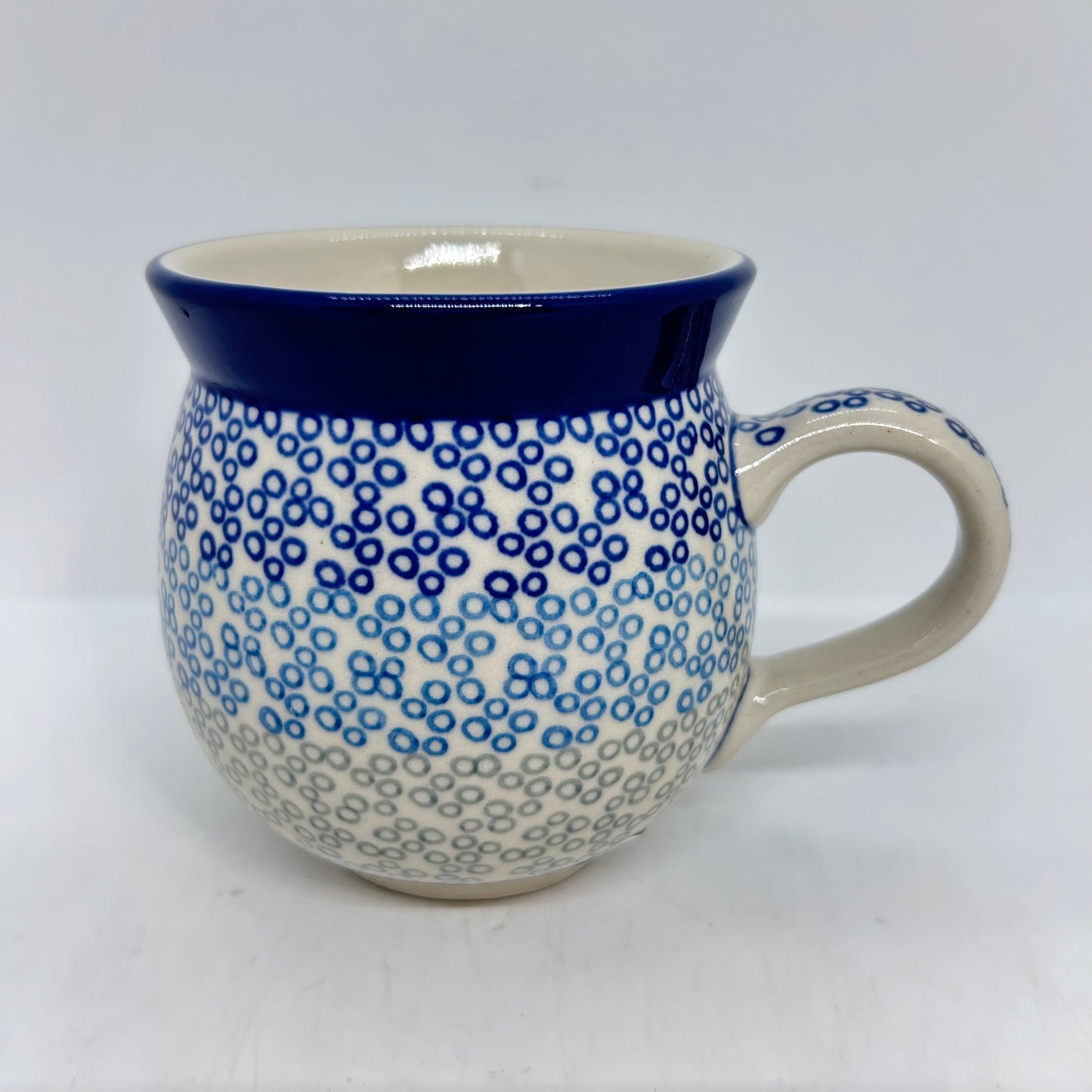 Straight-on side profile of a Ceramika Artystyczna Polish pottery bubble mug with the handle on the right, featuring a gradient pattern of blue and grey circular rings and a solid dark blue rim.