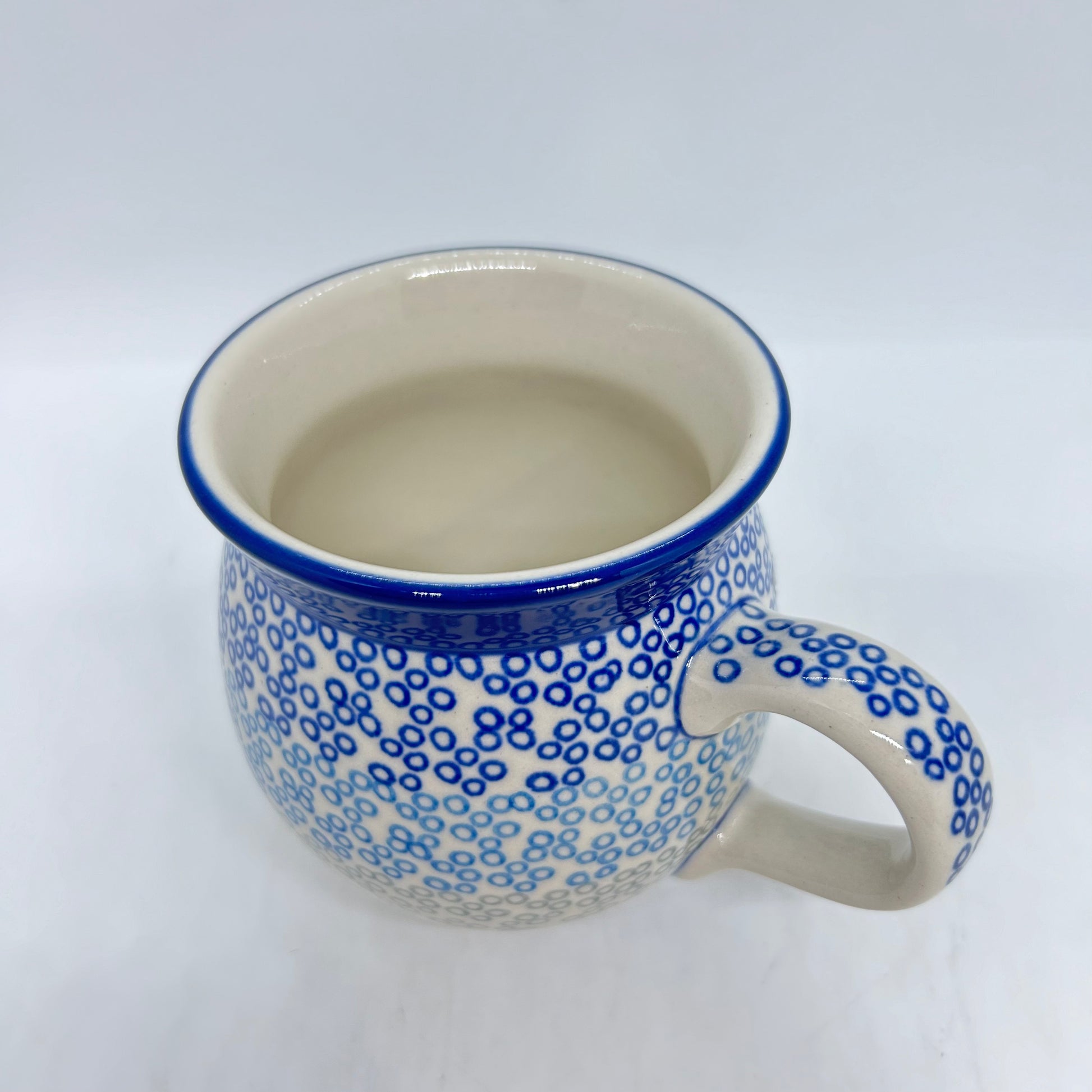 Elevated three-quarter view of a Ceramika Artystyczna Polish pottery bubble mug featuring a blue and grey gradient ring pattern reaching a thin blue rim, a patterned right handle, and a smooth off-white interior.
