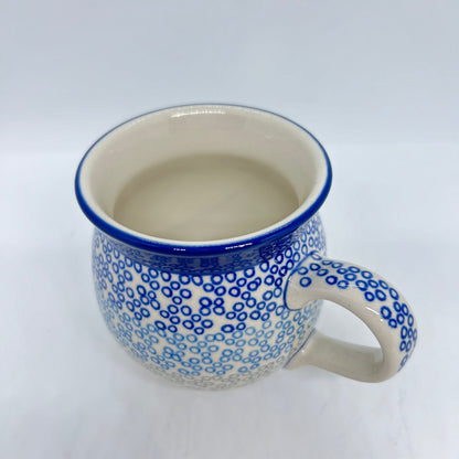 Elevated three-quarter view of a Ceramika Artystyczna Polish pottery bubble mug featuring a blue and grey gradient ring pattern reaching a thin blue rim, a patterned right handle, and a smooth off-white interior.