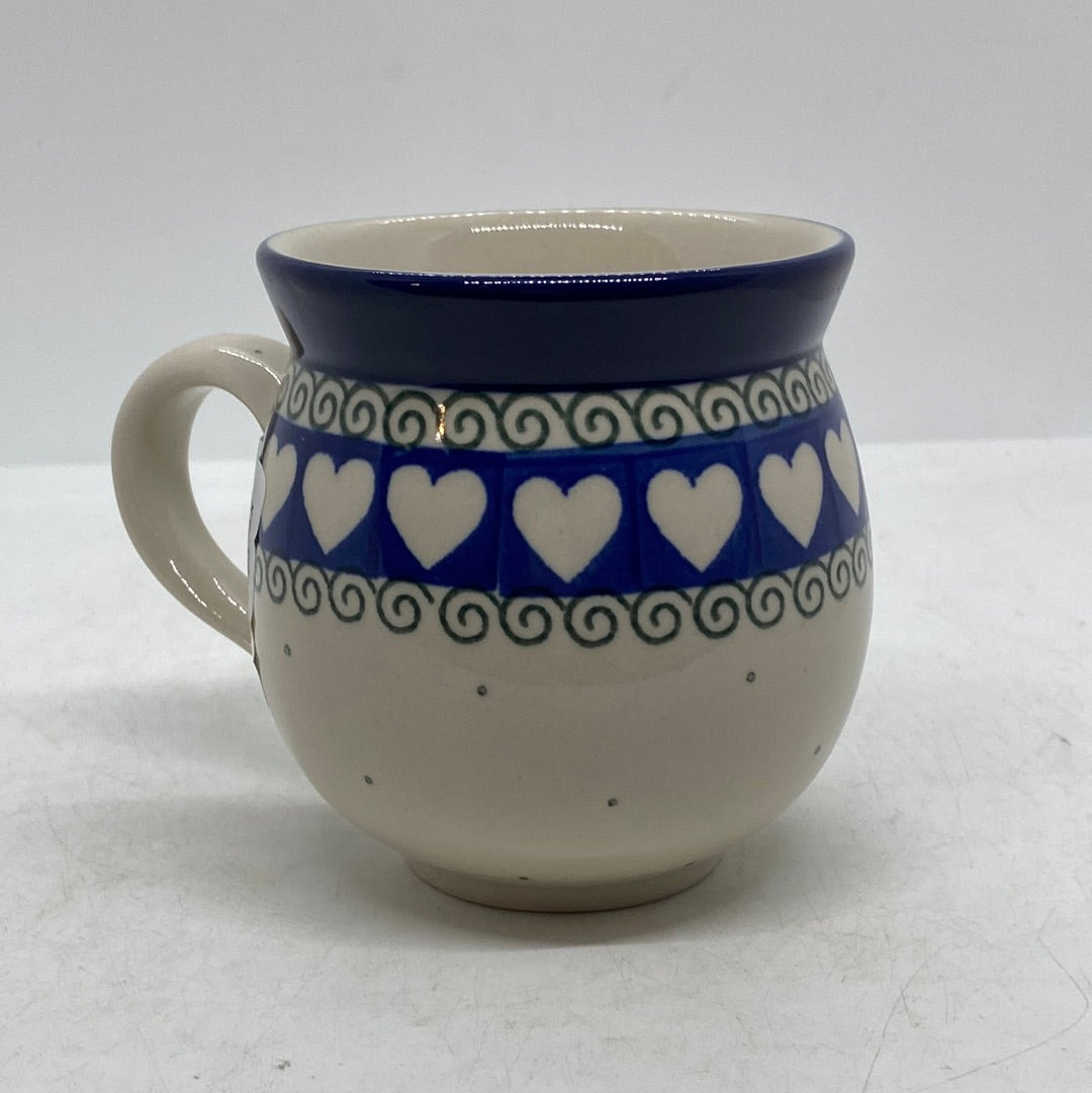 Side profile view of a Ceramika Artystyczna Polish pottery bubble mug with the handle on the left, featuring a band of white hearts on blue, green scroll borders, and a solid blue rim.