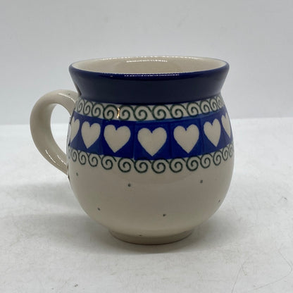 Side profile view of a Ceramika Artystyczna Polish pottery bubble mug with the handle on the left, featuring a band of white hearts on blue, green scroll borders, and a solid blue rim.