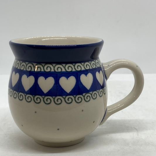 Side profile view of a Ceramika Artystyczna Polish pottery bubble mug with the handle on the right, featuring a band of white hearts on blue, green scroll borders, and a solid blue rim.