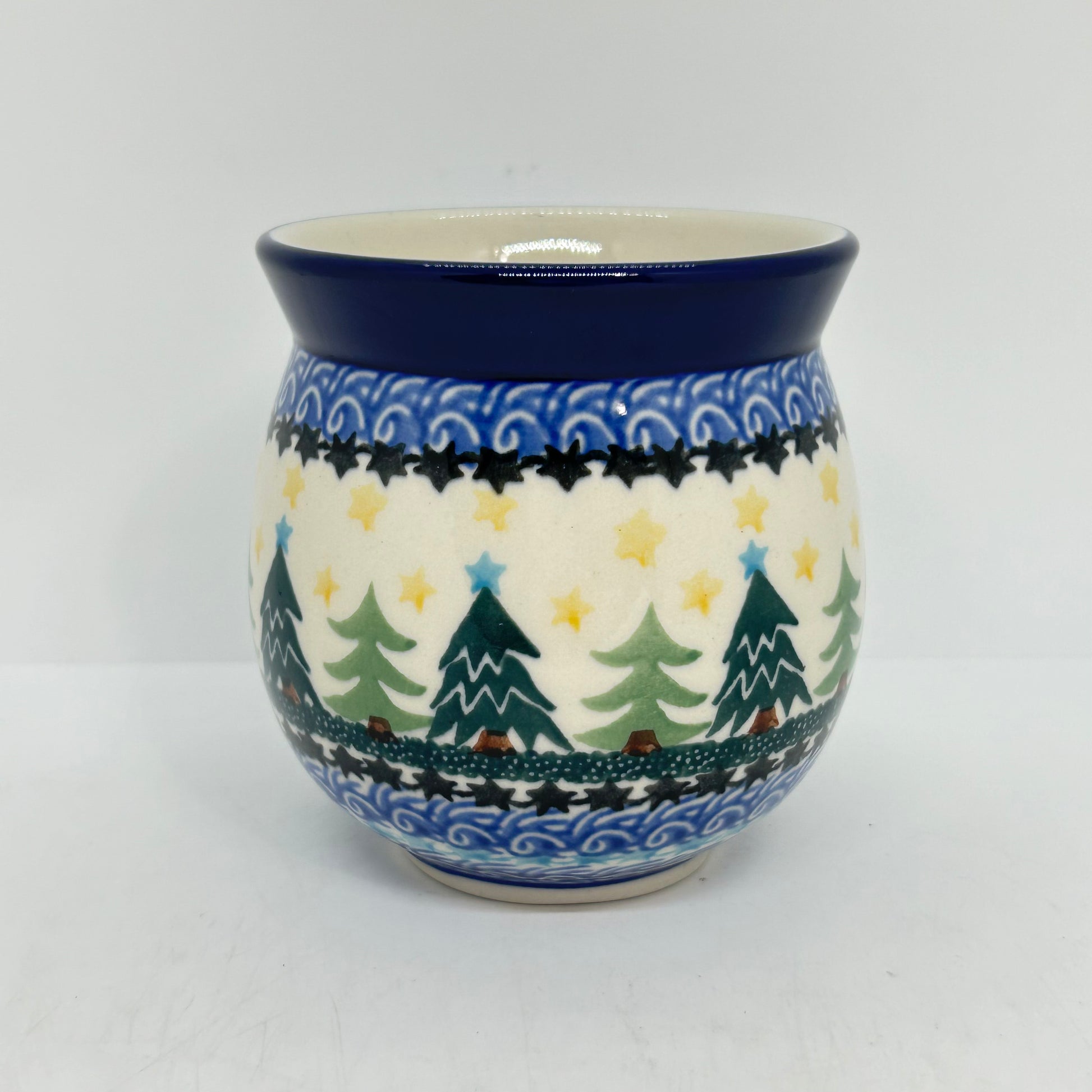 Straight-on view of the back of a Ceramika Artystyczna Polish pottery bubble mug, showing a continuous pattern of Christmas trees, yellow stars, layered star borders, and a solid dark blue rim with no handle visible.