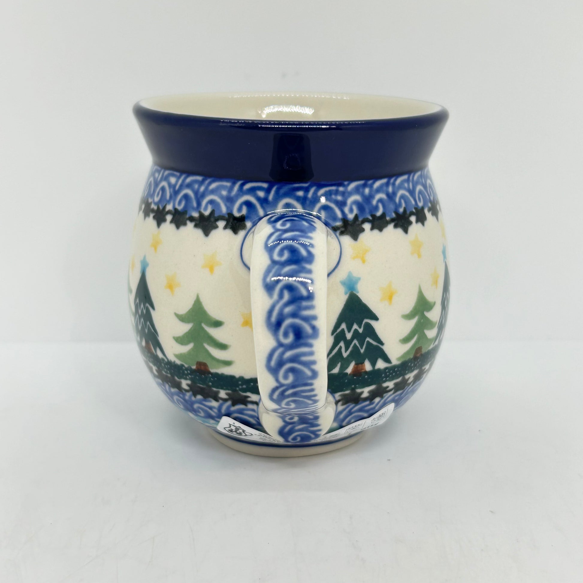 Straight-on view focusing on the patterned handle of a Ceramika Artystyczna Polish pottery bubble mug, flanked by Christmas trees, yellow stars, and complex layered borders.