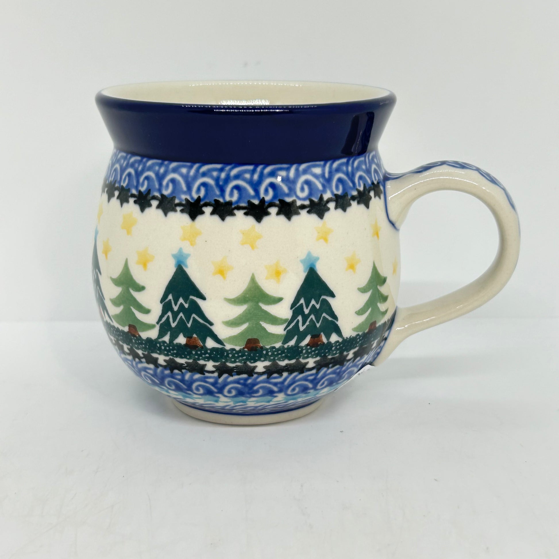 Straight-on side profile of a Ceramika Artystyczna Polish pottery bubble mug with the handle on the right, showing green Christmas trees, yellow stars, layered blue and black star borders, and a solid dark blue rim.