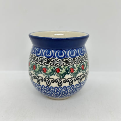 Straight-on view of the back of a Ceramika Artystyczna Polish pottery bubble mug, showing the continuous horizontal bands of blue wave motifs, black scrollwork, and green leaves with red berries without the handle visible.
