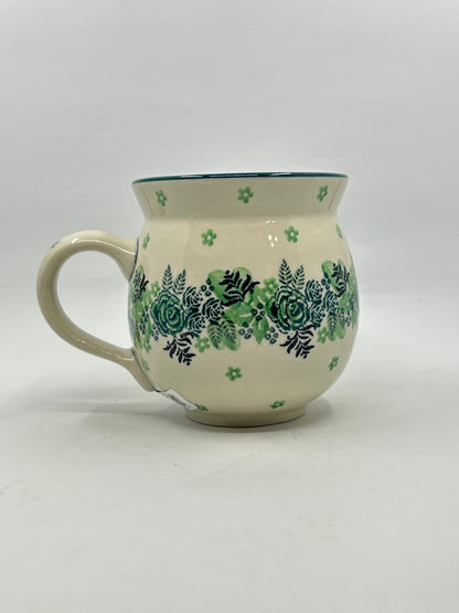 Side profile view of a Ceramika Artystyczna Polish pottery bubble mug with the handle on the left, displaying a continuous central band of green roses and dark ferns on a cream background.