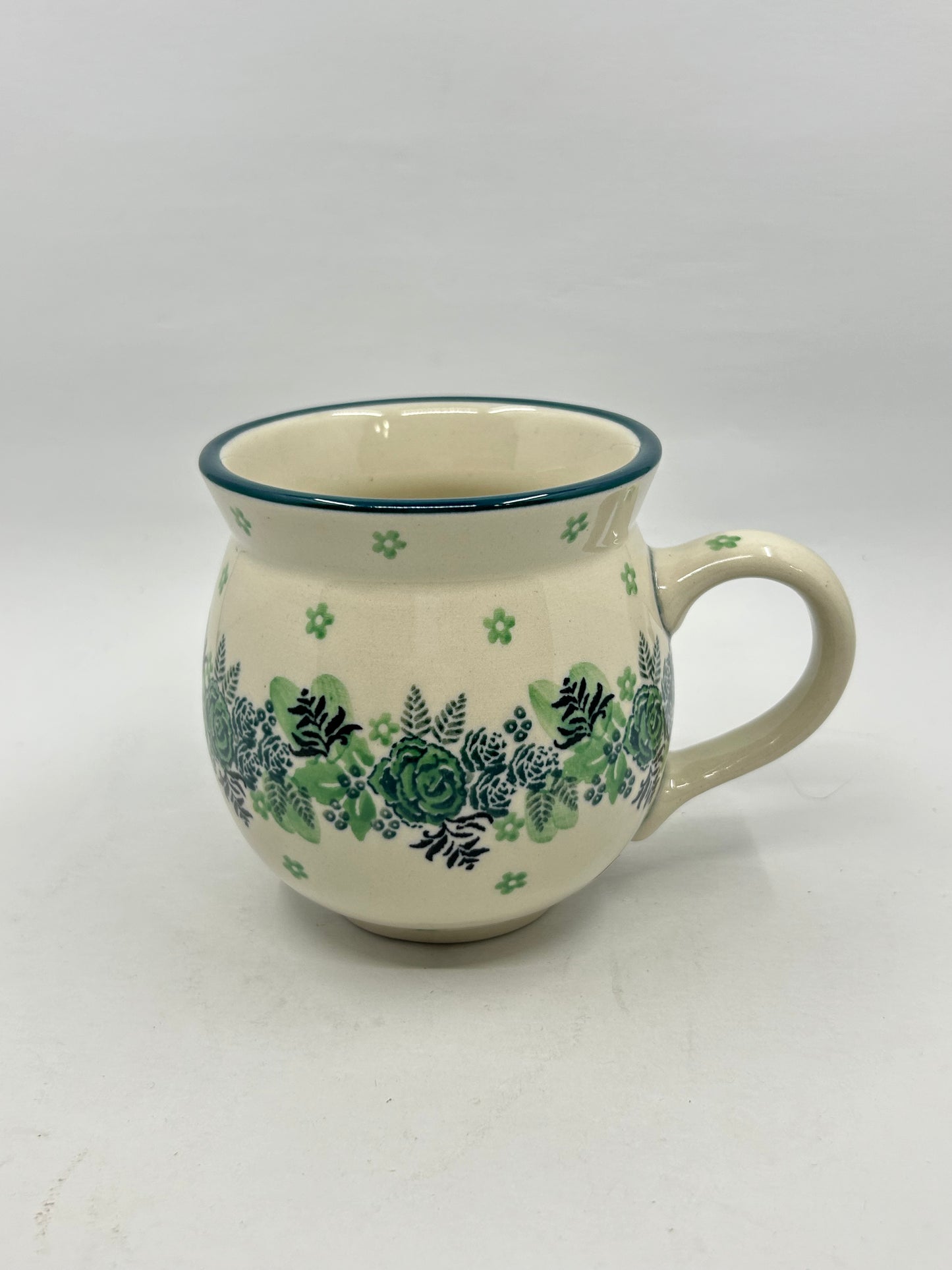 Elevated three-quarter view of a Ceramika Artystyczna Polish pottery bubble mug, highlighting the green rose and fern pattern, the thin green rim border, and a clear look into the smooth off-white interior.