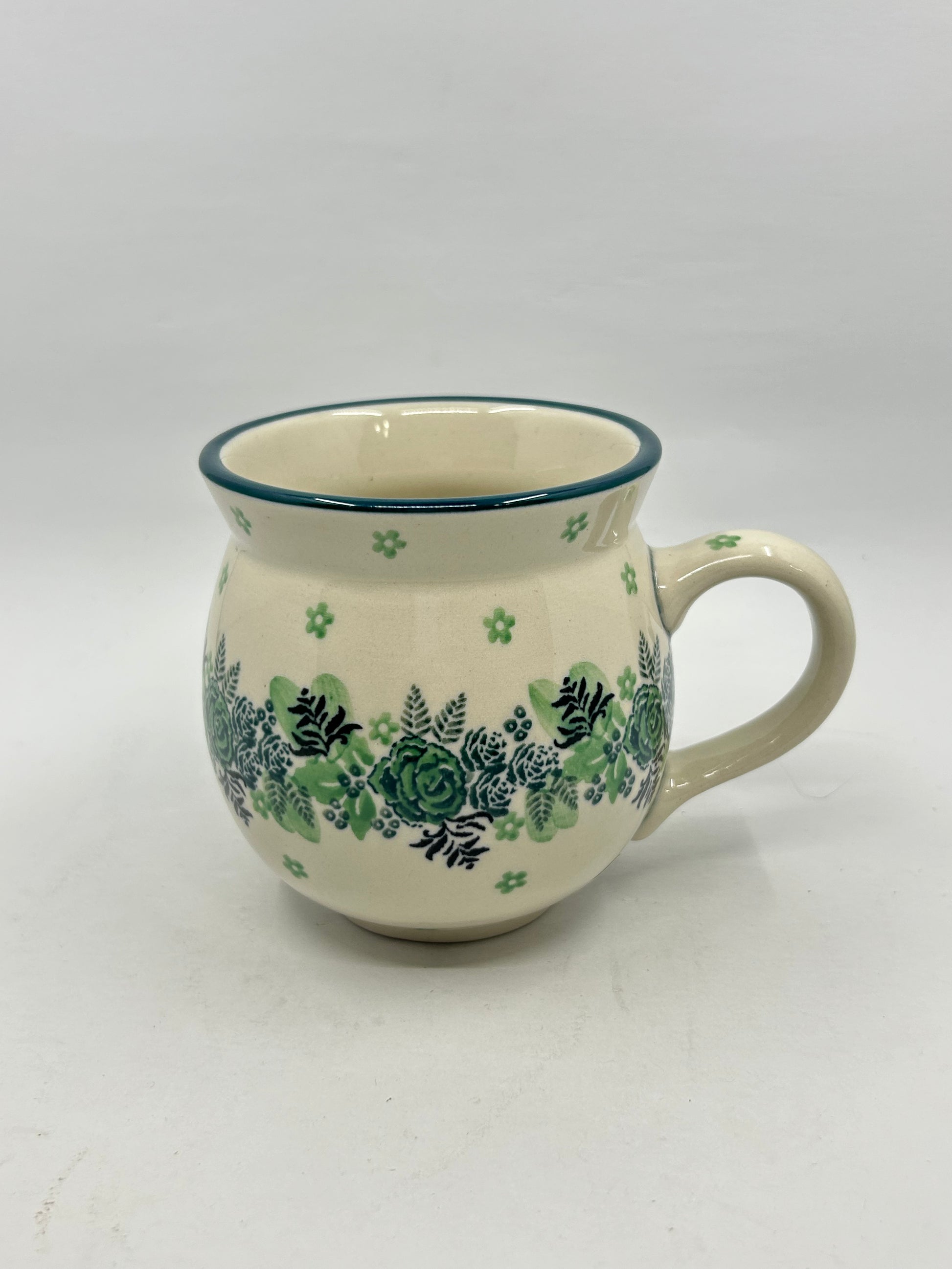 Elevated three-quarter view of a Ceramika Artystyczna Polish pottery bubble mug, highlighting the green rose and fern pattern, the thin green rim border, and a clear look into the smooth off-white interior.