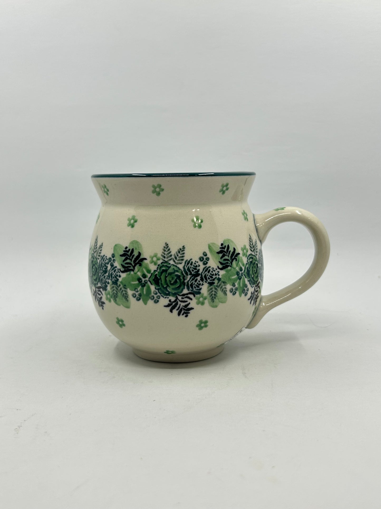 Side profile view of a Ceramika Artystyczna Polish pottery bubble mug featuring a central horizontal band of green roses and dark ferns, accented by small scattered green flowers on a cream background.