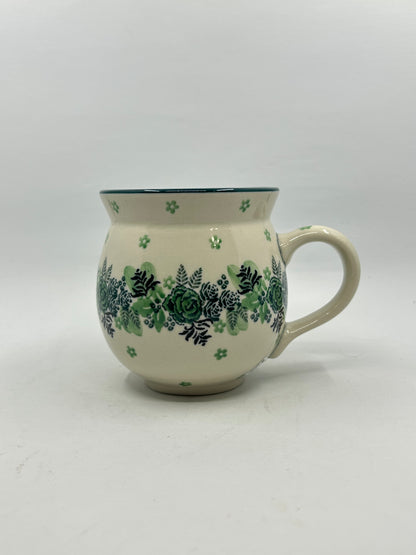 Side profile view of a Ceramika Artystyczna Polish pottery bubble mug featuring a central horizontal band of green roses and dark ferns, accented by small scattered green flowers on a cream background.