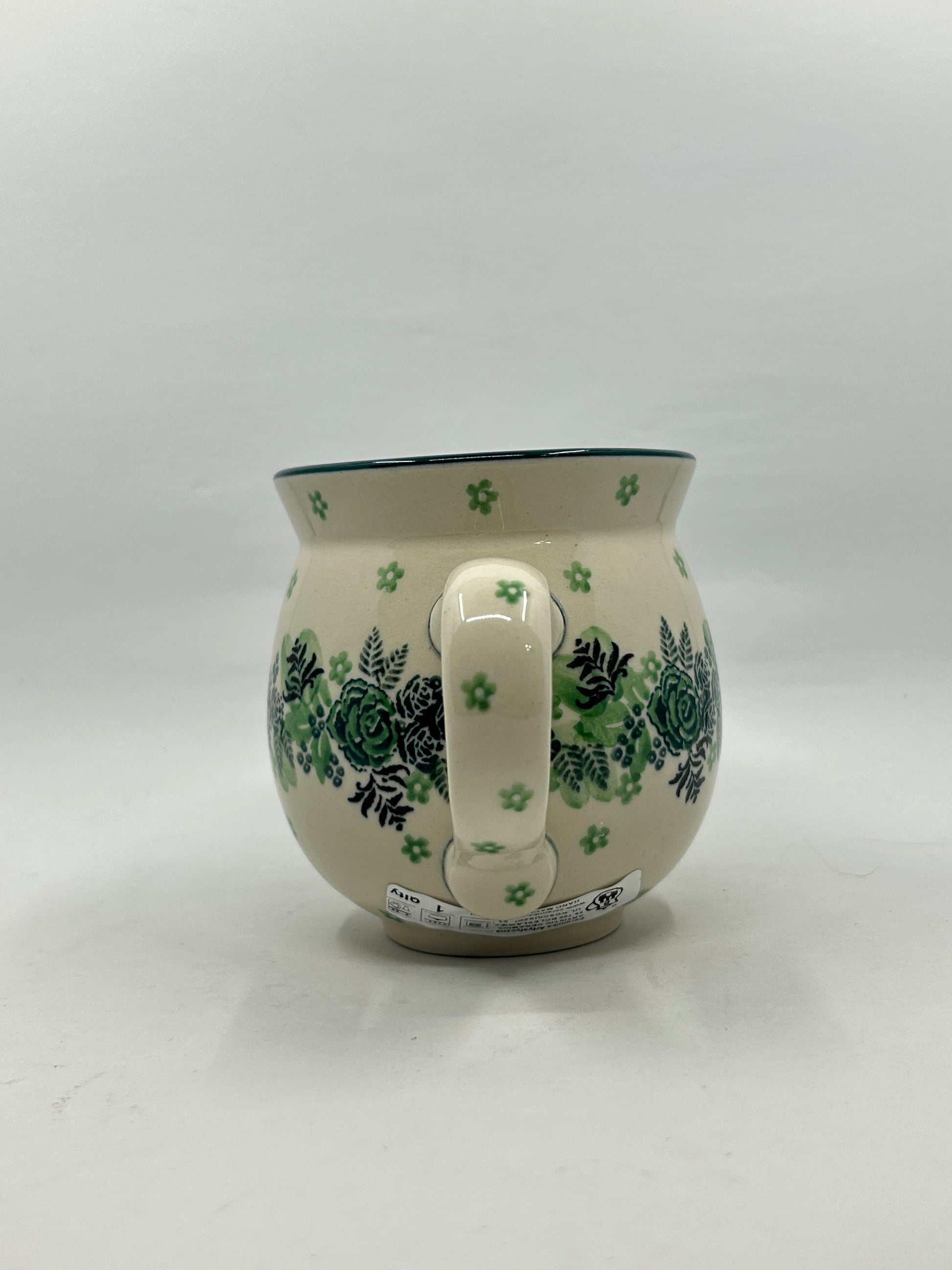 Straight-on view of the handle of a Ceramika Artystyczna Polish pottery bubble mug, showing green flower stamps on the handle and the botanical rose and fern pattern wrapping around both sides.