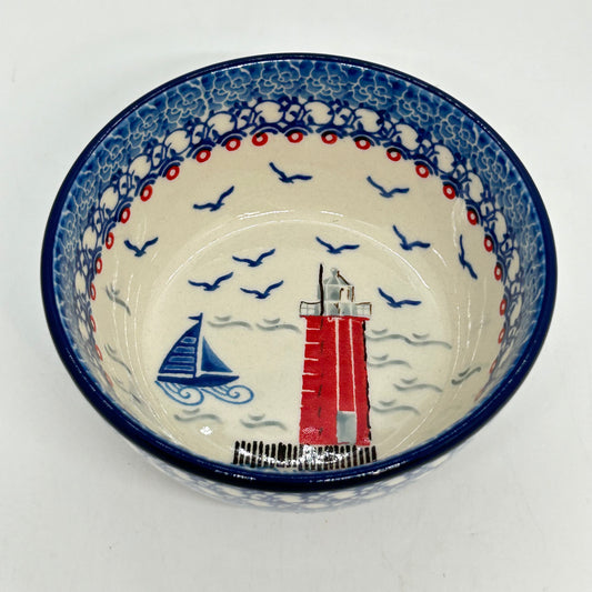 Elevated angled view looking into a Ceramika Artystyczna Polish pottery cereal bowl, featuring a hand-painted nautical lighthouse and sailboat scene on the interior floor, surrounded by flying seagulls and a traditional blue and white stamped border.