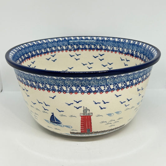 Front-facing view of a Ceramika Artystyczna Polish pottery serving bowl showing the dark blue rim, traditional blue and white stamped borders, and a hand-painted nautical lighthouse and sailboat scene.
