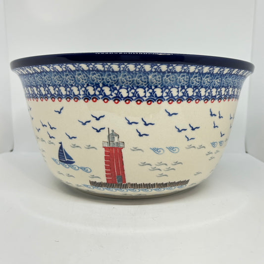 Straight-on profile view of a Ceramika Artystyczna Polish pottery serving bowl featuring a traditional blue and white stamped border, dark blue rim, and a hand-painted nautical lighthouse and sailboat scene.