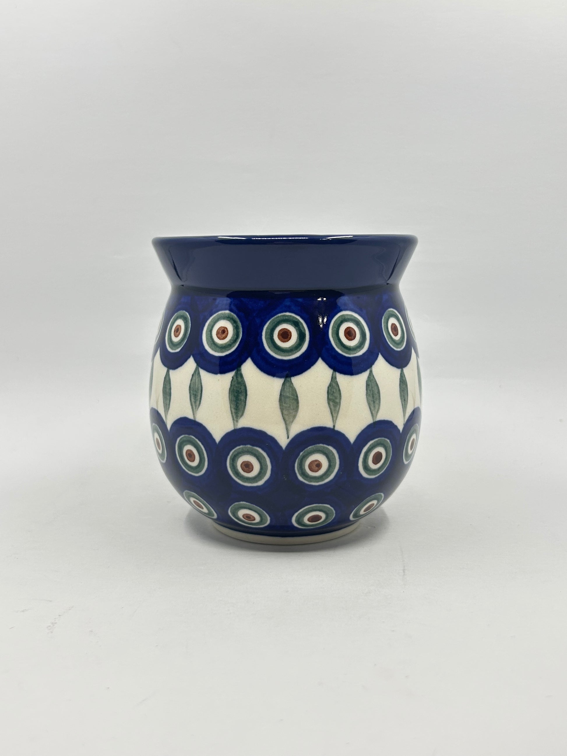Straight-on view of the back of a Ceramika Artystyczna Polish pottery bubble mug, showing a continuous pattern of the traditional Peacock Eye design with vertical green leaves, a solid dark blue rim, and no handle visible.