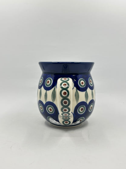 Straight-on view focusing on the patterned handle of a Ceramika Artystyczna Polish pottery bubble mug, flanked by the traditional Peacock Eye design, vertical green leaves, and a solid dark blue rim.
