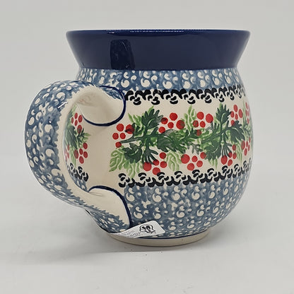 Straight-on side profile of a Ceramika Artystyczna Polish pottery bubble mug with the handle on the left, featuring a central band of red berries and green leaves, blue geometric stamping, and a solid dark blue rim.