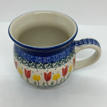 Elevated front view of a Ceramika Artystyczna Polish pottery bubble mug, showing a clean cream interior, a blue stamped handle, and hand-stamped red and yellow tulips framed by green vines.