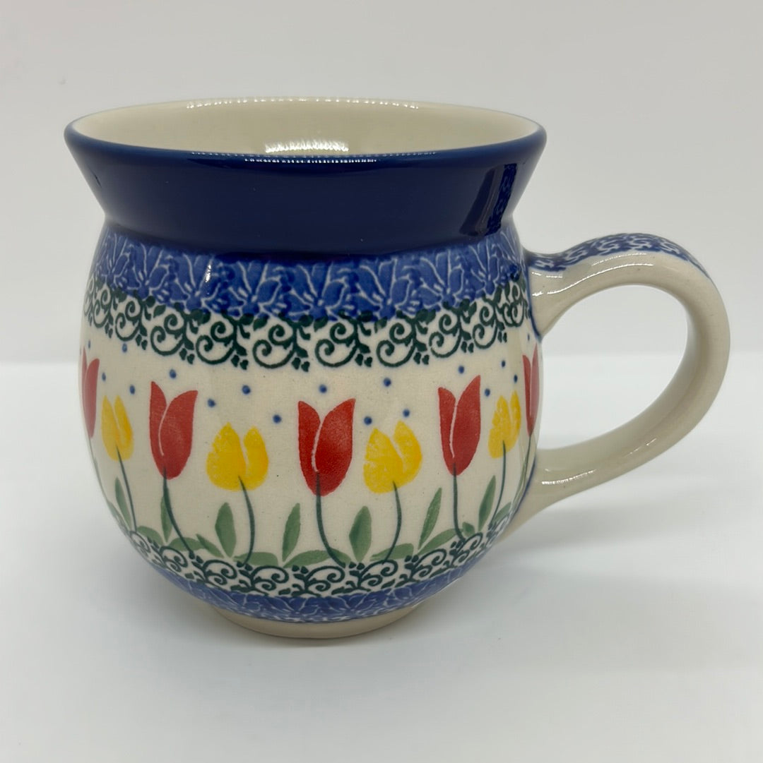 Elevated view of a Ceramika Artystyczna Polish pottery bubble mug, showing a clean cream interior, solid dark blue rim, a patterned handle, and an exterior featuring hand-painted red and yellow tulips framed by green vines and blue stamping.