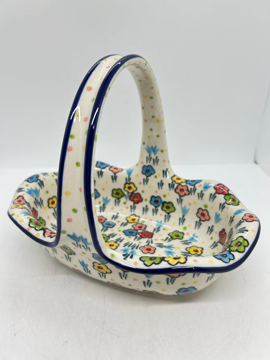 Slightly elevated view of a Ceramika Artystyczna Polish pottery basket with a fixed handle, featuring dark blue edge lines and hand-painted multi-colored spring flowers covering the interior basin and handle.