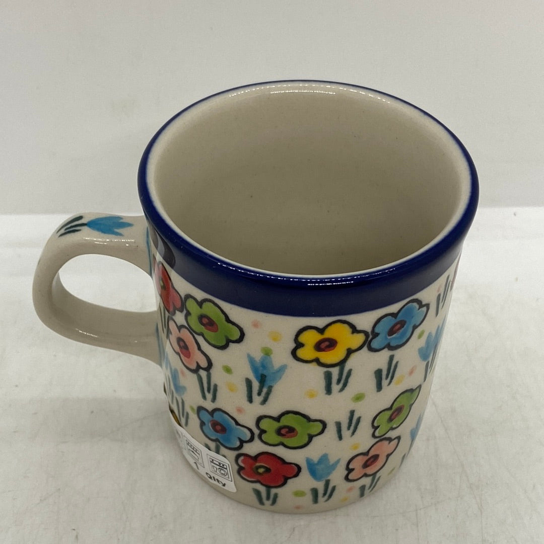 High-angle view looking inside a Ceramika Artystyczna Polish pottery coffee mug, showing a dark blue rim band, a decorated handle, and exterior spring flowers.