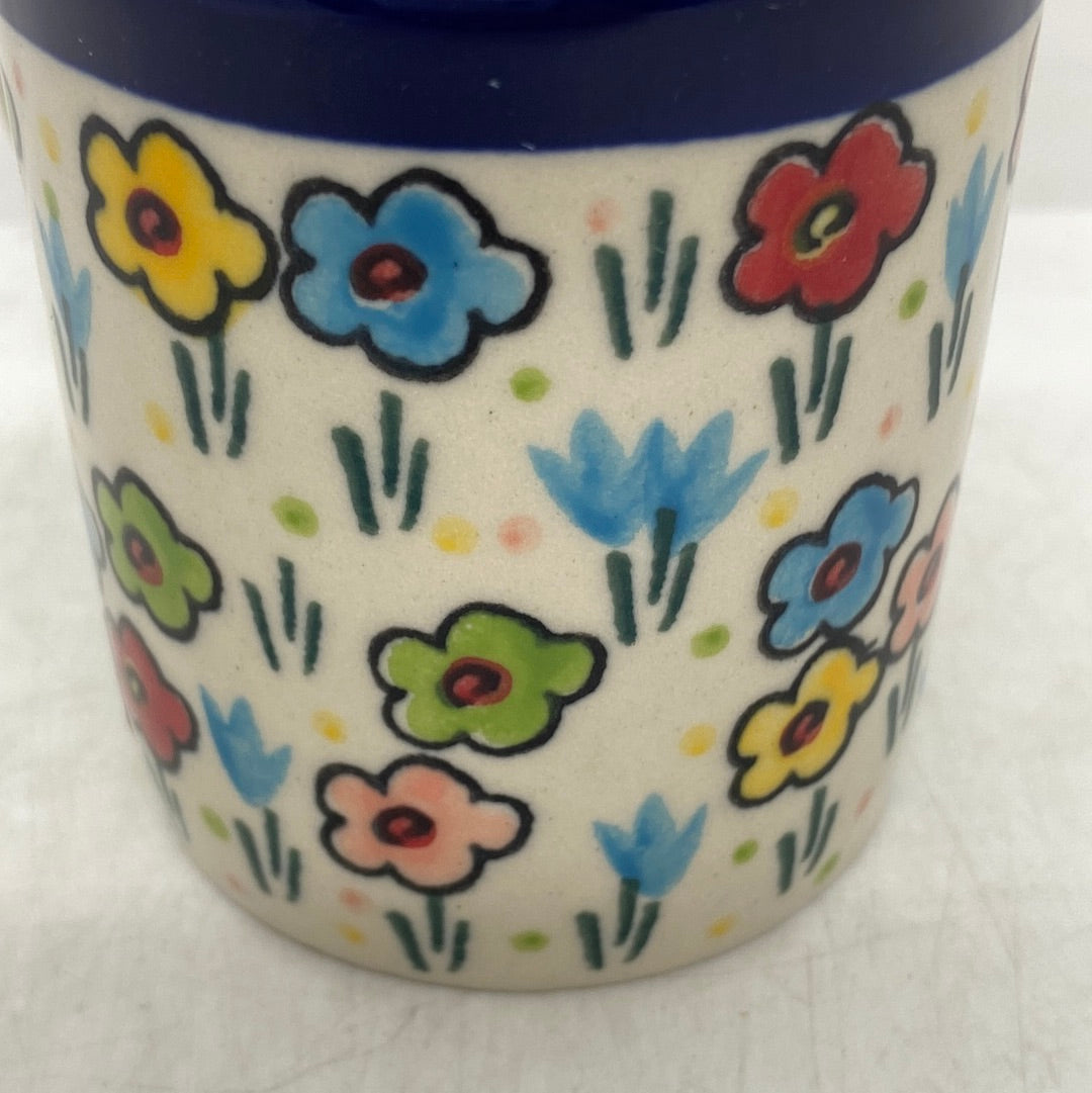 Macro close-up of a Ceramika Artystyczna Polish pottery coffee mug showing hand-painted spring flowers, green stems, and a glossy protective glaze beneath the blue rim.