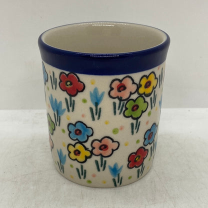 Side profile of a Ceramika Artystyczna Polish pottery coffee mug showing the handle-free side, a dark blue rim band, and hand-painted multi-colored spring flowers wrapping around the exterior.