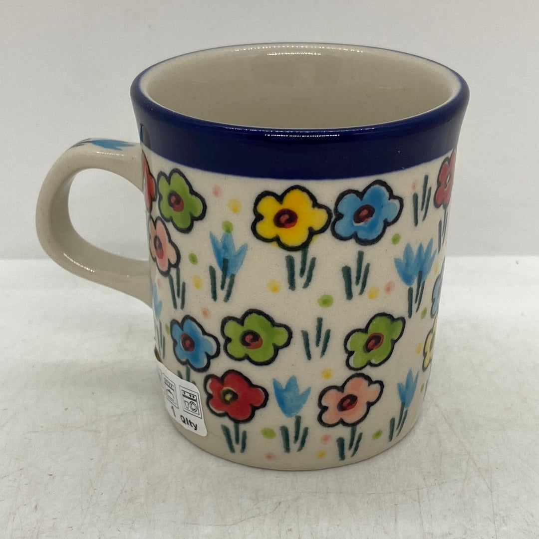 Straight-on side profile of a Ceramika Artystyczna Polish pottery coffee mug, featuring a dark blue band on the rim, a side handle, and hand-painted multi-colored spring flowers wrapping around the exterior.