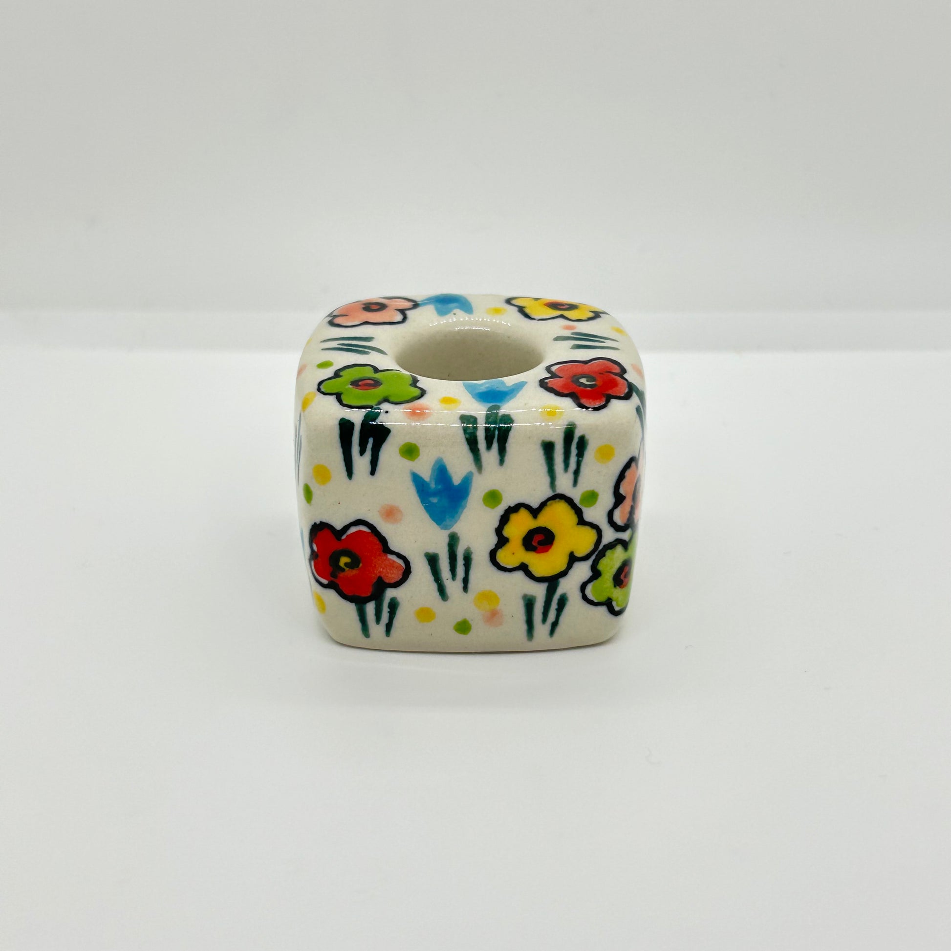Side profile view of a Ceramika Artystyczna Polish pottery cube-shaped taper candle holder showing the cuboid block, top candle socket, and hand-painted spring flowers.